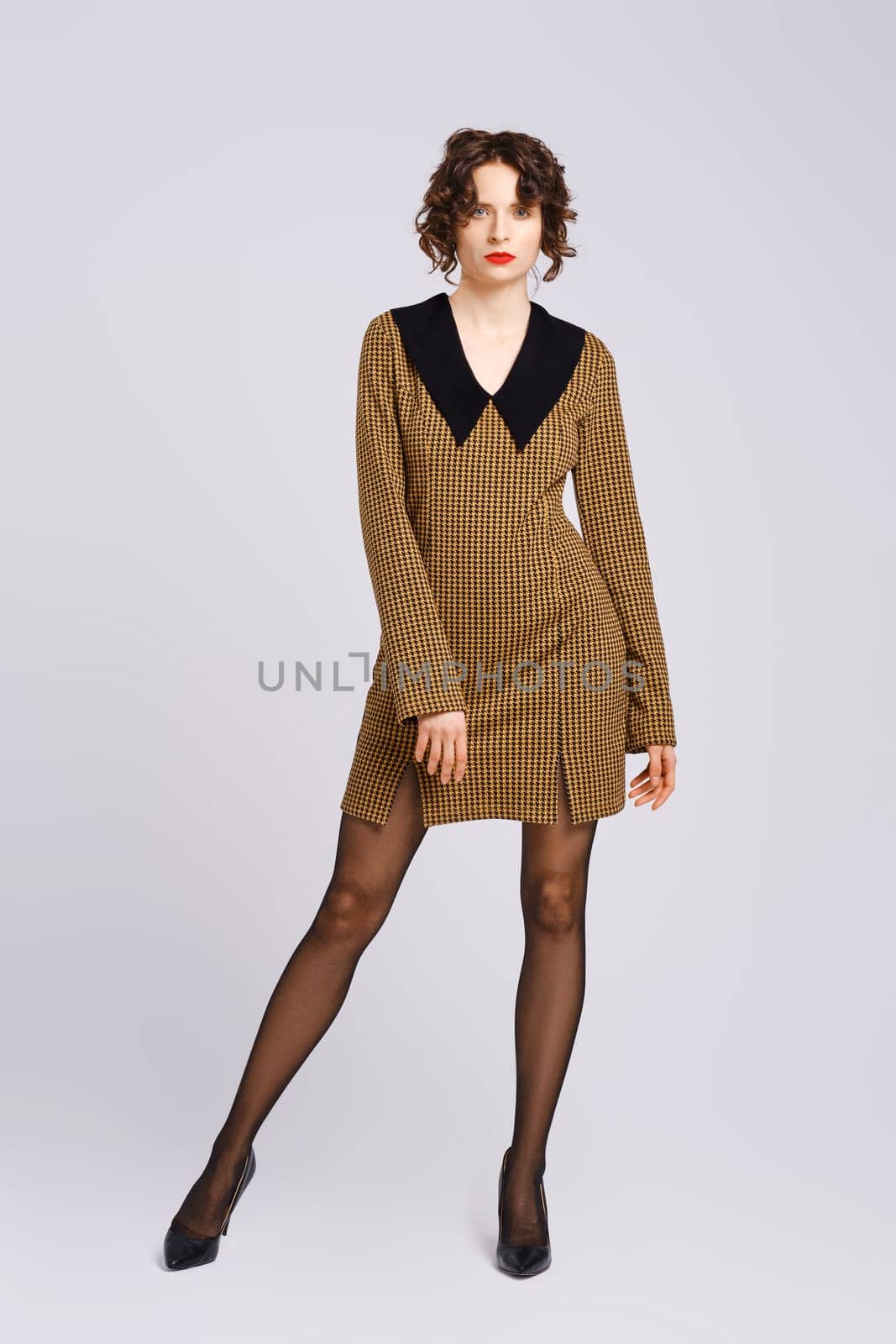 Trendy adult woman posing in grey studio in short dress with big collar
