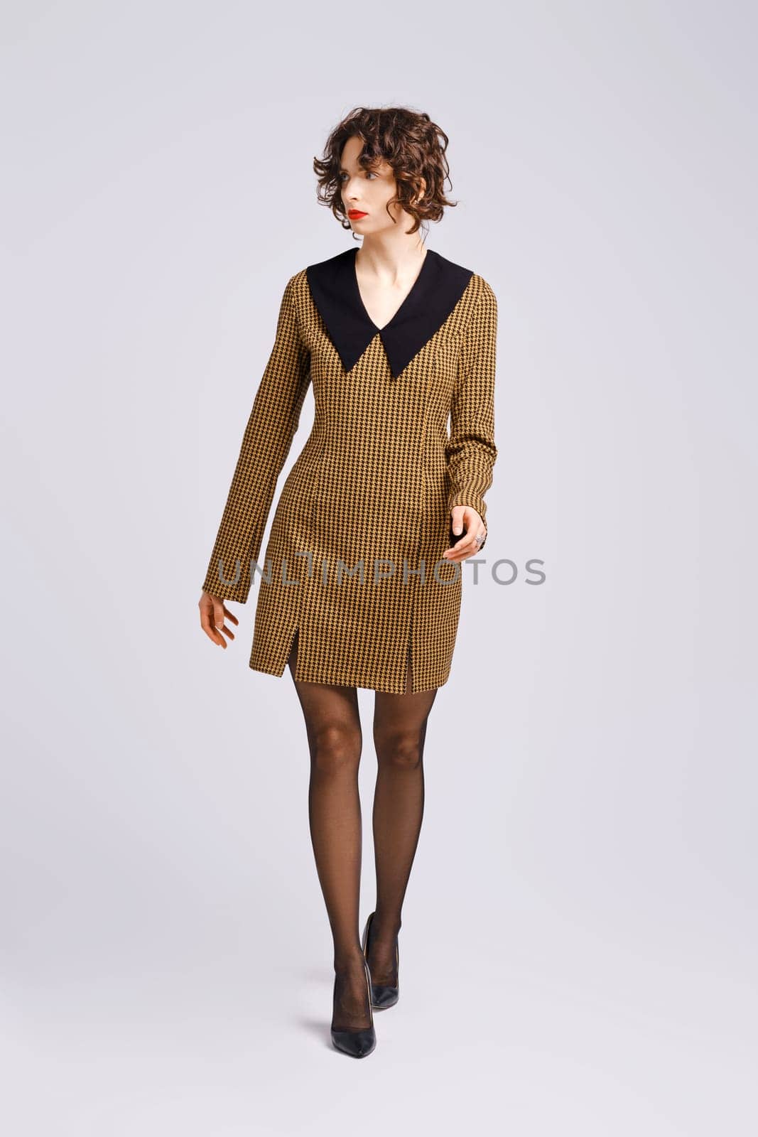 Woman in dress with large collar walks forward in studio and looking to the side