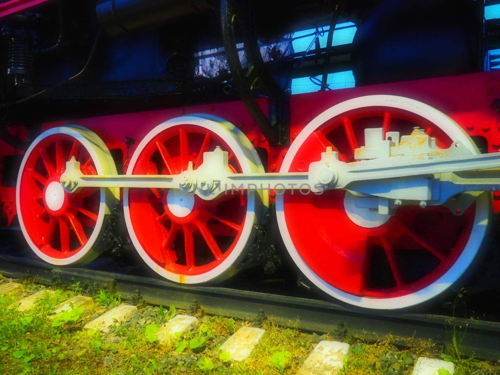 Retro vintage wheels of a locomotive or train close up. Red large heavy metal wheels with piston guiding mechanisms. Locomotive of the 19th - 20th centuries with a steam engine. Bright vivid photo.