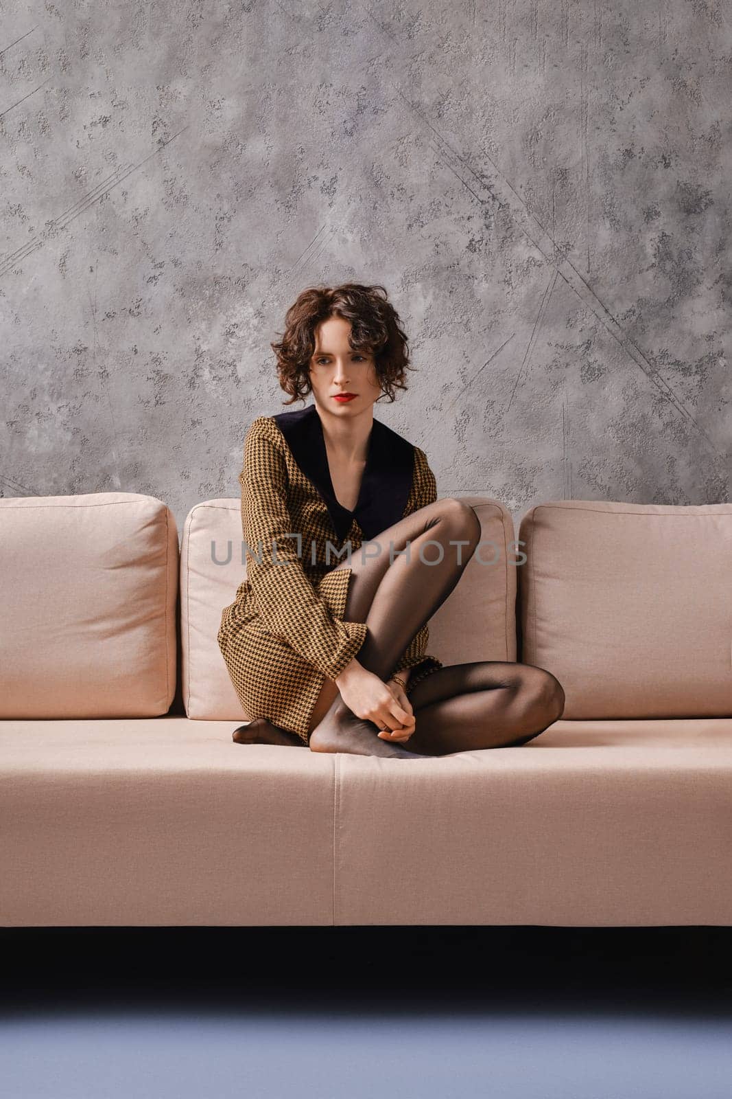 Lonely and sad young woman sits on couch with her legs crossed
