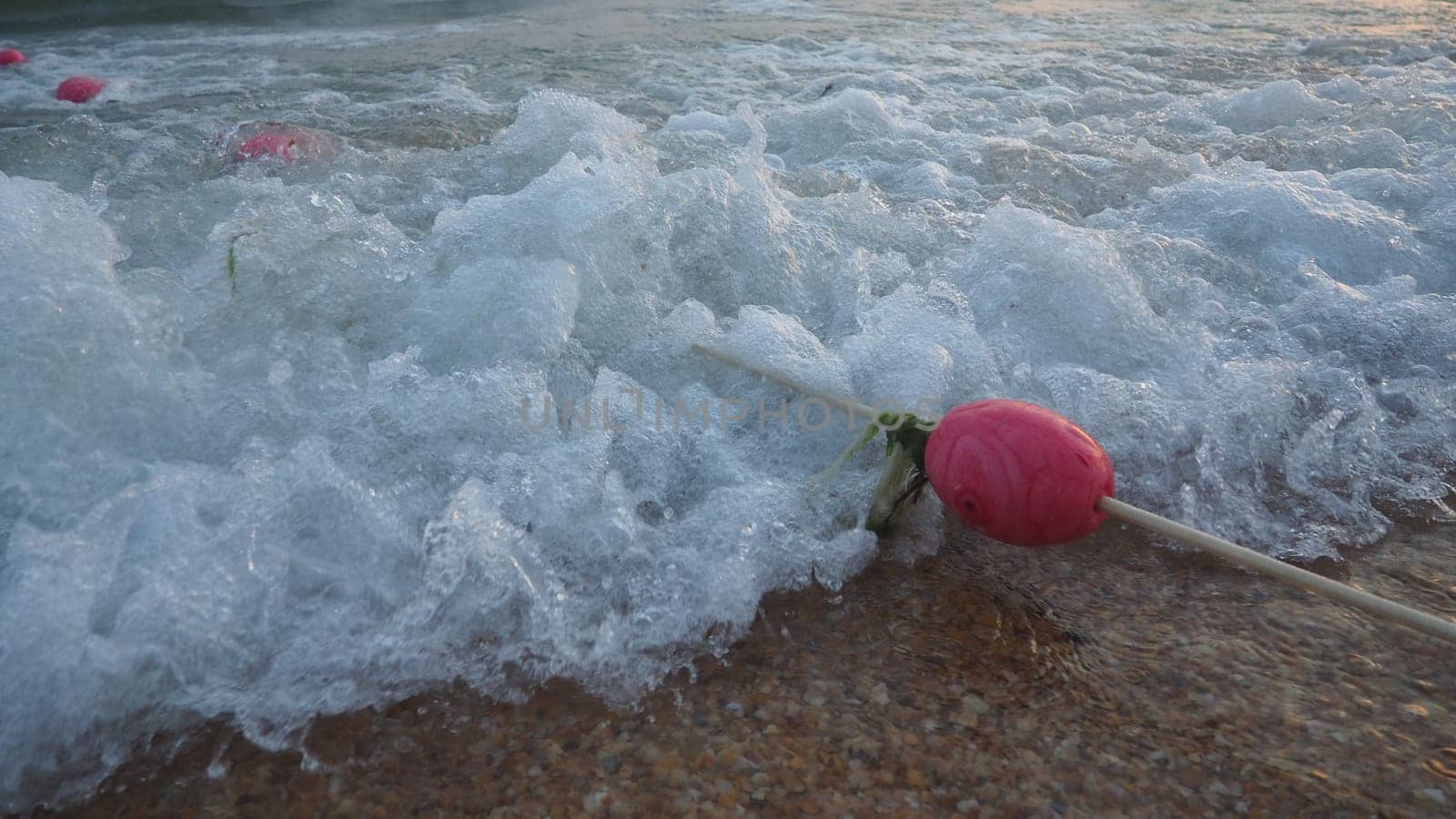 Buoys on a rope near sea water. The buoys are pink restraints to alert people to the depth of the water. Rescue of the drowning. Delimiting a place on a sandy beach between hotels. Wave with bubbles