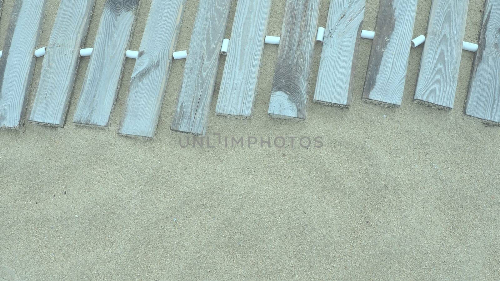 Wooden footbridge on a sandy beach. Uneven, damp wooden planks held together. The edge of the beach season at the hotel. No people, copy space. Equipped sandy beach after a storm or cyclone. Tourism.