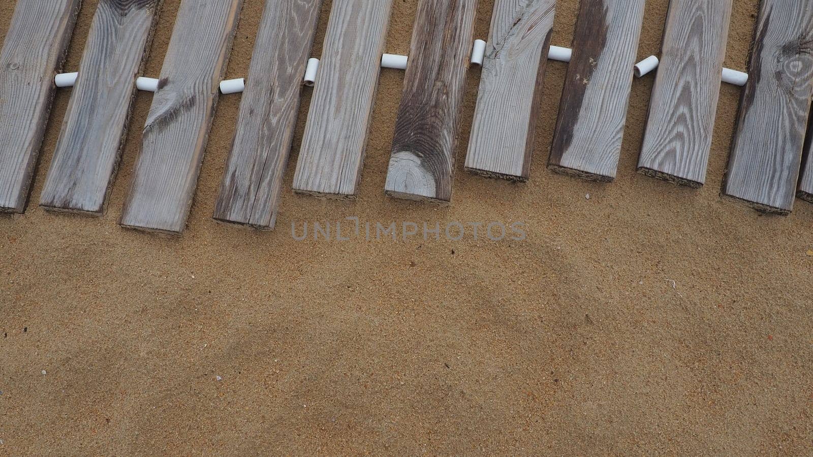 Wooden footbridge on a sandy beach. Uneven, damp wooden planks held together. The edge of the beach season at the hotel. No people, copy space. Equipped sandy beach after a storm or cyclone. Tourism.