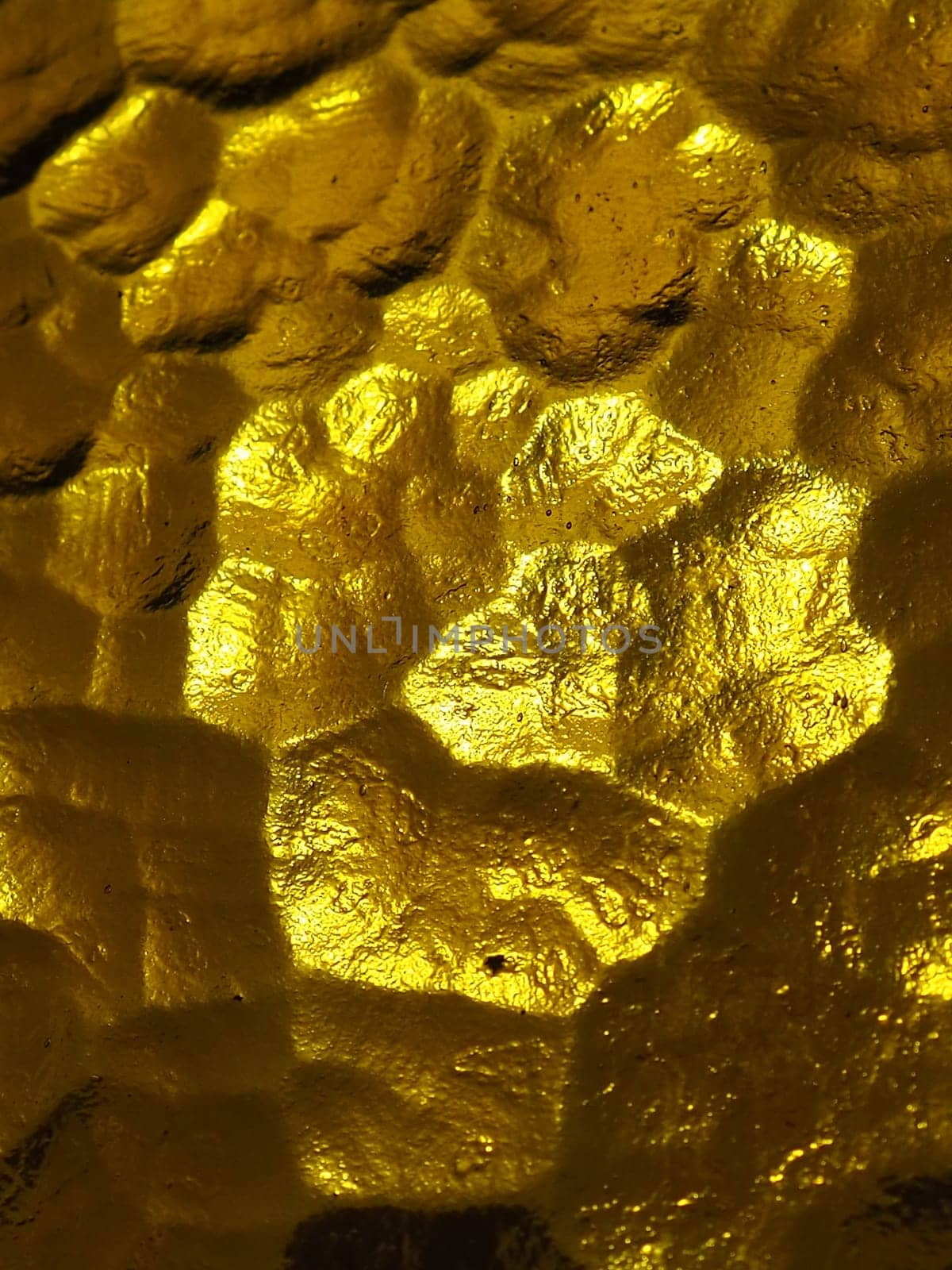 golden yellow corrugated glass with a light and dark background. reflections of light. Corrugated glass, rear light source. Play of glare and reflections on a transparent uneven surface