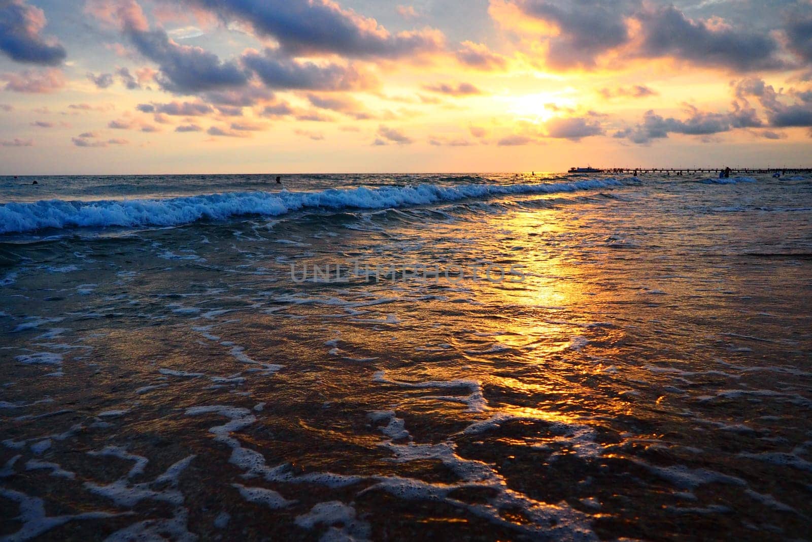 Wave and sunset over sea. Beautiful sunset. Foamy waves roll over the sandy shore. Vityazevo, Anapa, Black Sea. Tourist mecca, health resort. Evening sky. The rays reflect off the water.