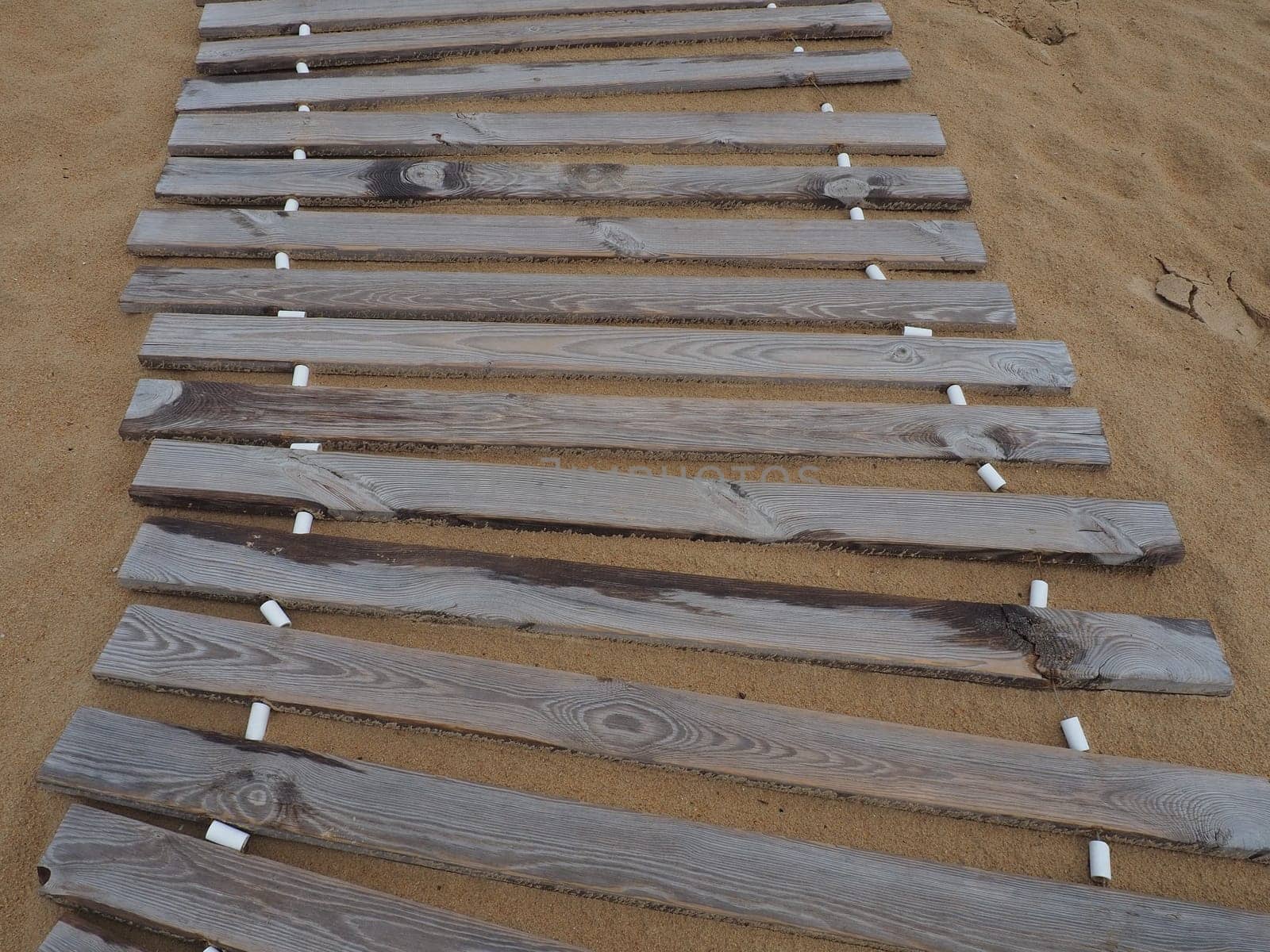 Wooden footbridge on a sandy beach. Uneven, damp wooden planks held together. The edge of the beach season at the hotel. No people, copy space. Equipped sandy beach after a storm or cyclone. Tourism.