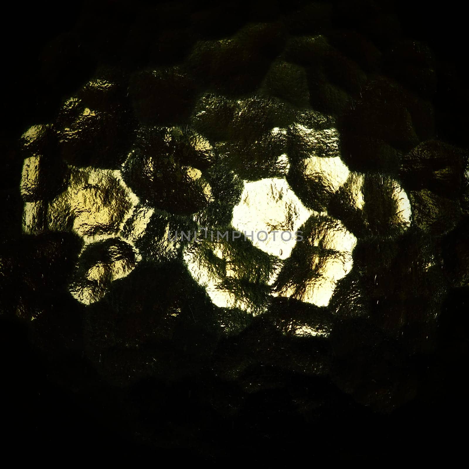 Corrugated glass, rear light source. Play of glare and reflections on a transparent uneven surface. Dark and light abstract asymmetric multi-illuminated planes. Abstract bumpy golden background