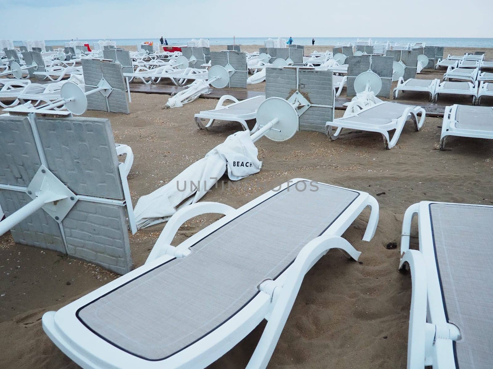A beach umbrella lay folded on a sandy beach after bad weather. Storm at sea. End of the beach season due to typhoon and cyclone. Loungers, umbrellas and hotel furniture. Wind-upturned structures.