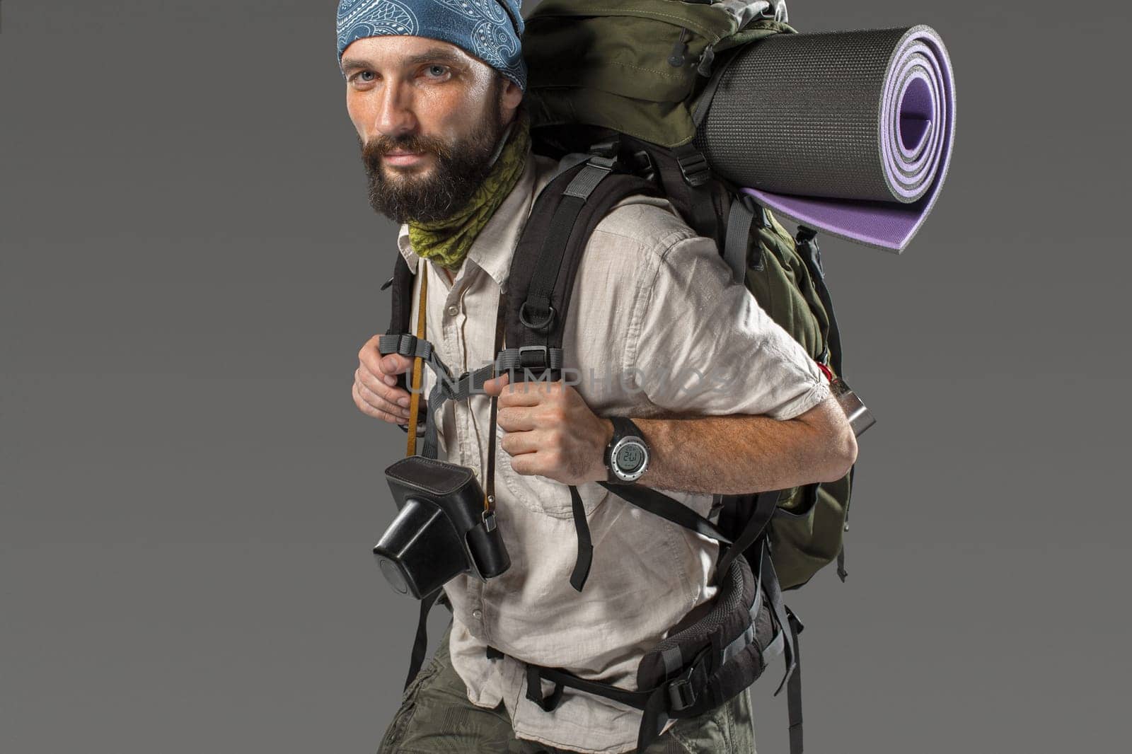 Portrait of a male fully equipped tourist with backpack and the camera on gray background