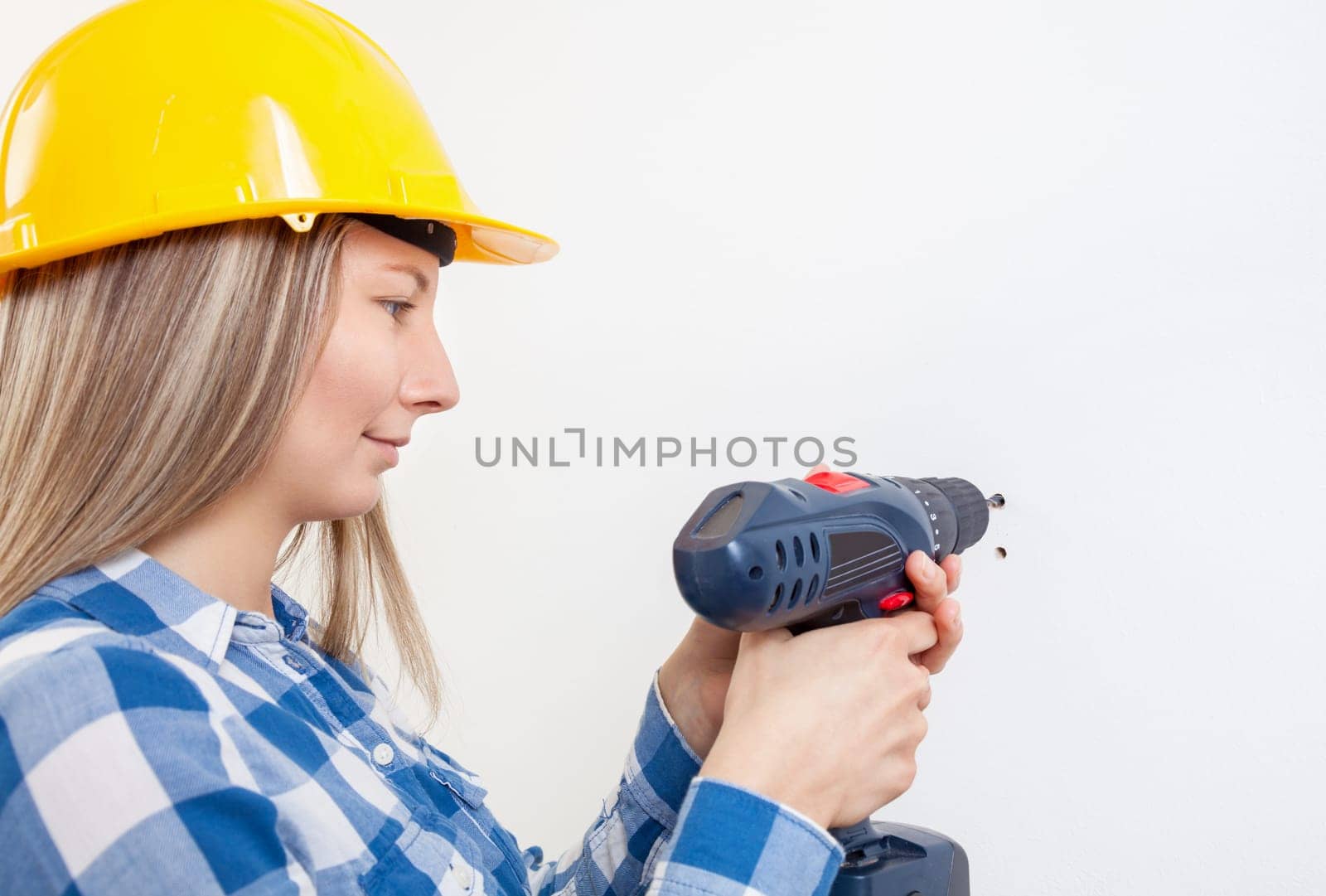Young woman drilling a hole in the wall and wearing a protective helmet