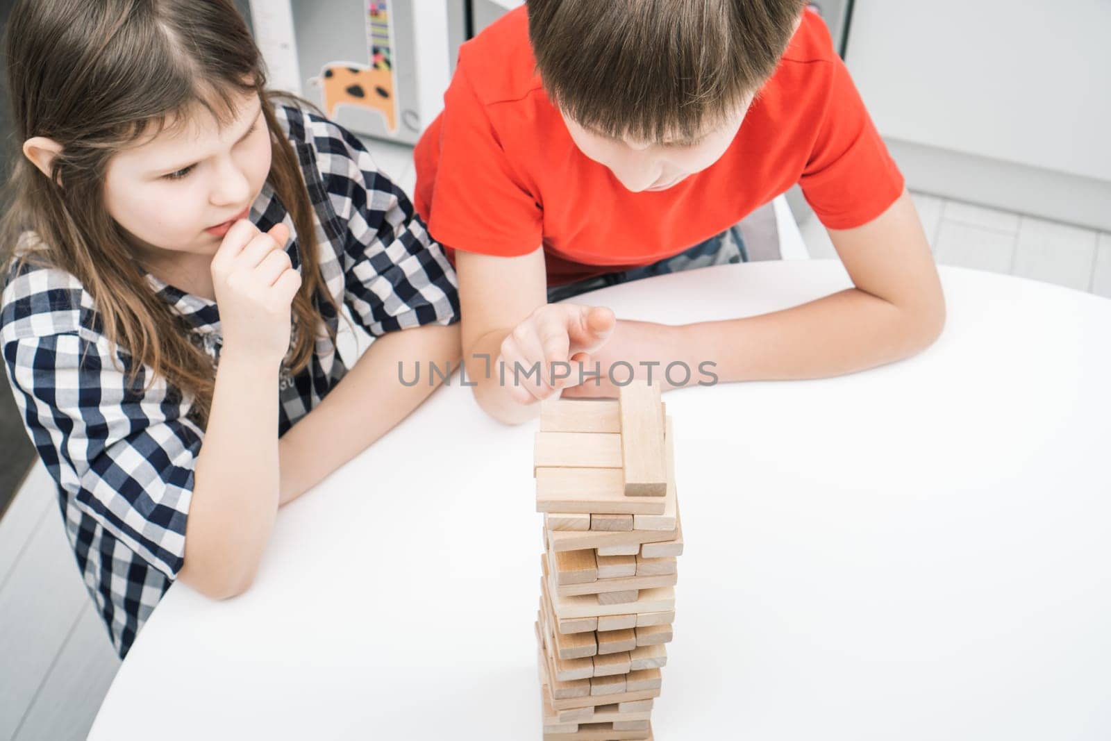 Serious, concentrated children, boy and girl thinking of strategy in board wooden brick tower game. Moving blocks carefully from pyramids on table. Smart and logical board games. High angle view