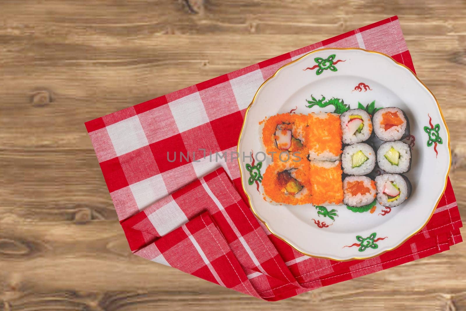 Traditional japanese sushi menu. Various kinds of sushi rolls with salmon, sashimi served on a colorful plate on red checkered napkin on rustic table. Top view. Space.