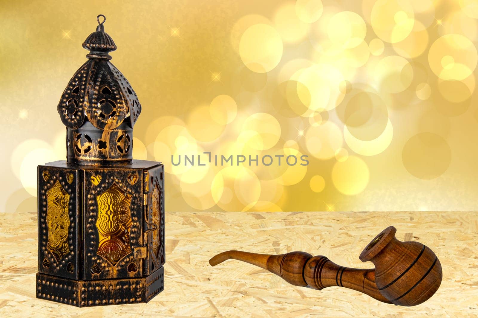 Old oriental or arabic metallic lantern and a handmade wooden tobacco pipe on table over abstract golden stars background. Ramadan Kareem template. Card design.