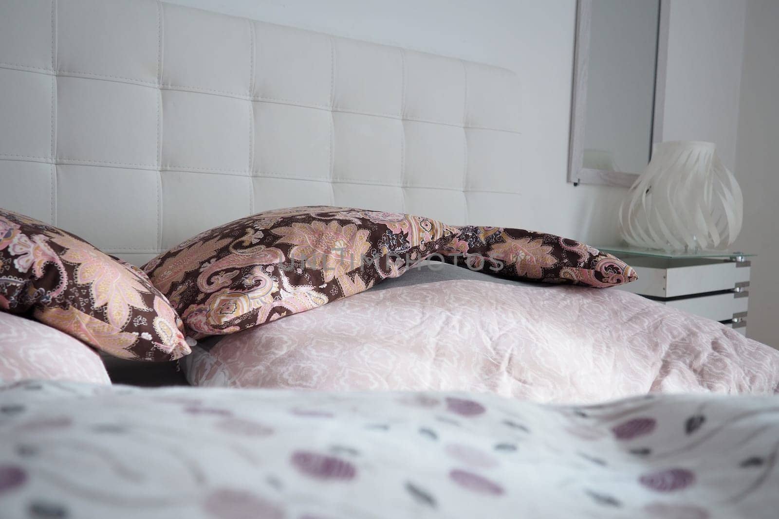 Pink decorative pillows on the bed linen. Double bridal bed with pillows and thick feather duvet. Bedroom design. Soft white headboard. Interior with furniture and bedding