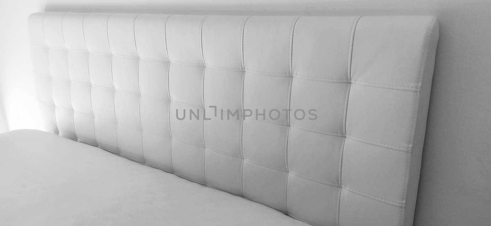 Soft headboard. Upholstery for furniture made of genuine or artificial leather and quilted fabric. Soft headboard against a light wall. Black and white monochrome photo.