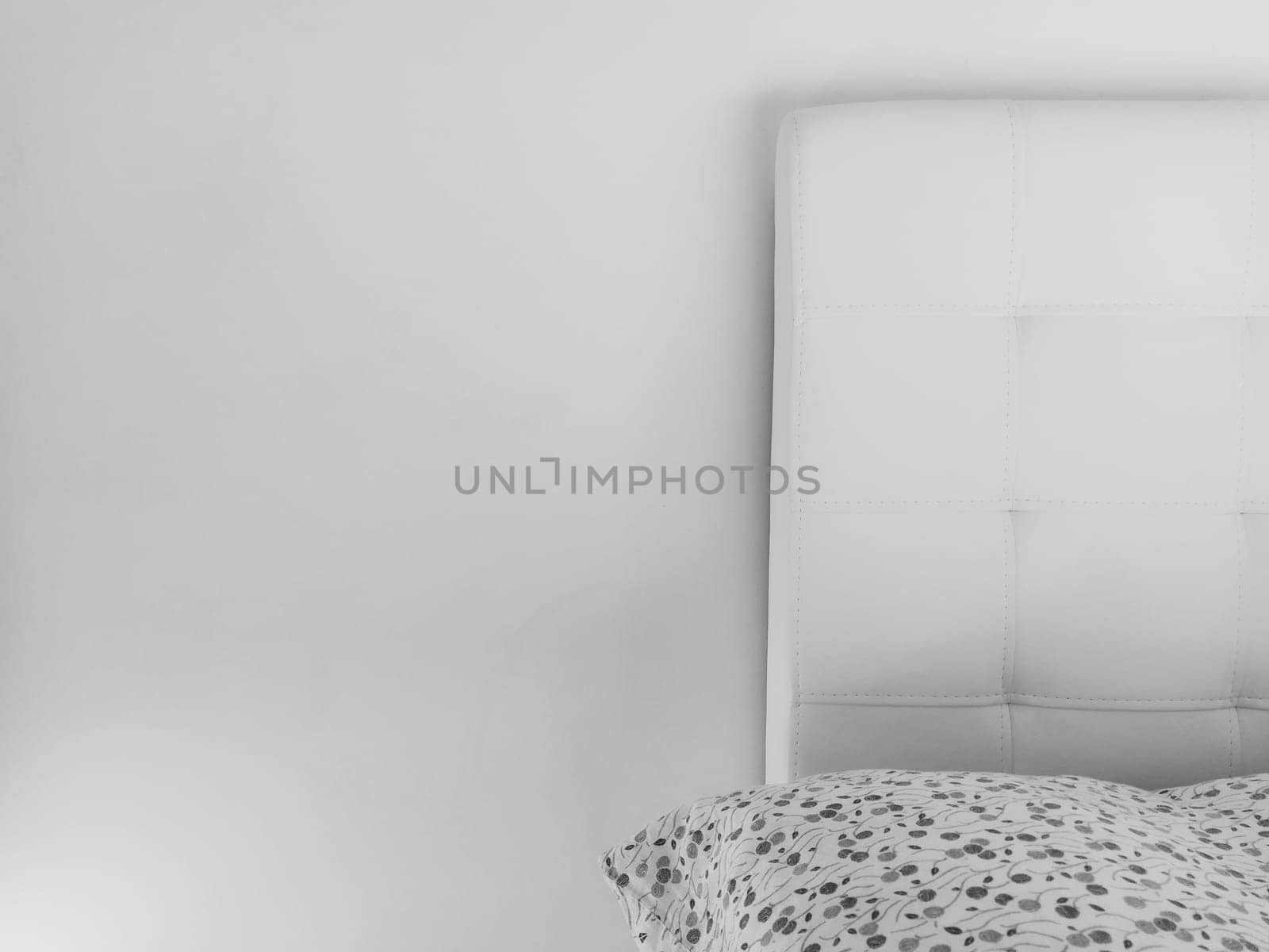 Soft headboard. Upholstery for furniture made of genuine or artificial leather and quilted fabric. Soft headboard against a light wall. Black and white monochrome photo.