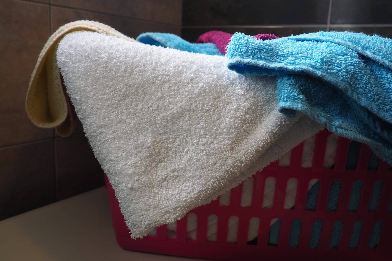 Towels in the laundry basket. Blue and pink cotton terry towels are thrown into a pink plastic basket. Housekeeping. Storing and separating laundry before washing. Light from above from an open window