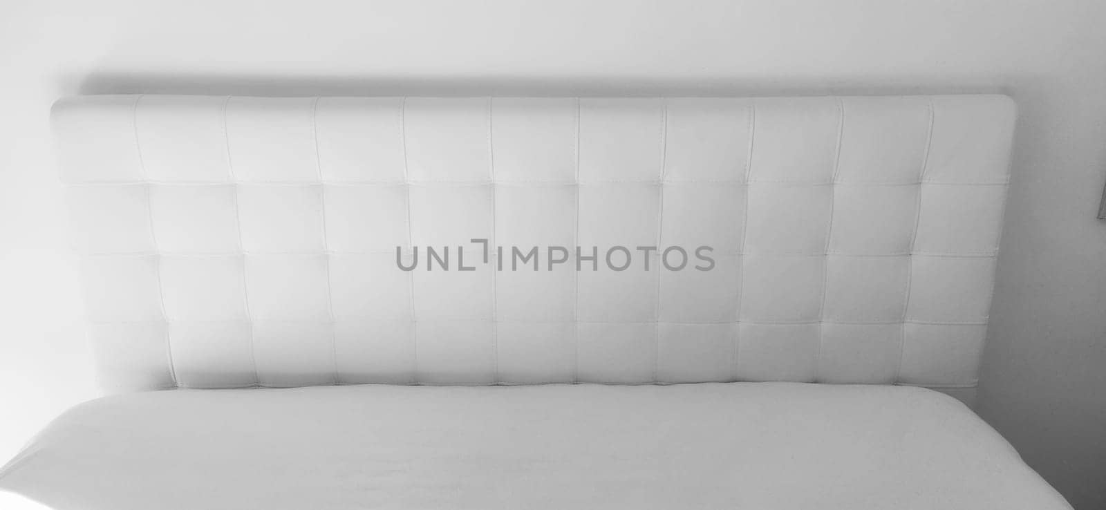 Soft headboard. Upholstery for furniture made of genuine or artificial leather and quilted fabric. Soft headboard against a light wall. Black and white monochrome photo.