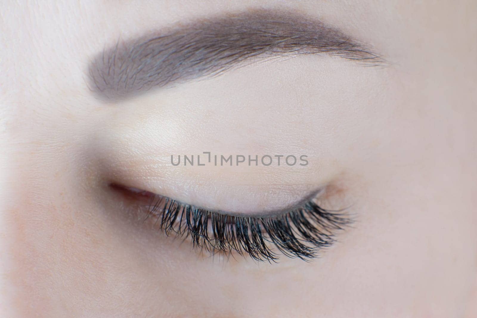 Close-up of closed eye with long magnificent eyelashes, black eyeliner, healthy skin, ideal eyebrow of unrecognizable young woman. Macro. Lash extension, beauty procedures, cosmetology, microblading.