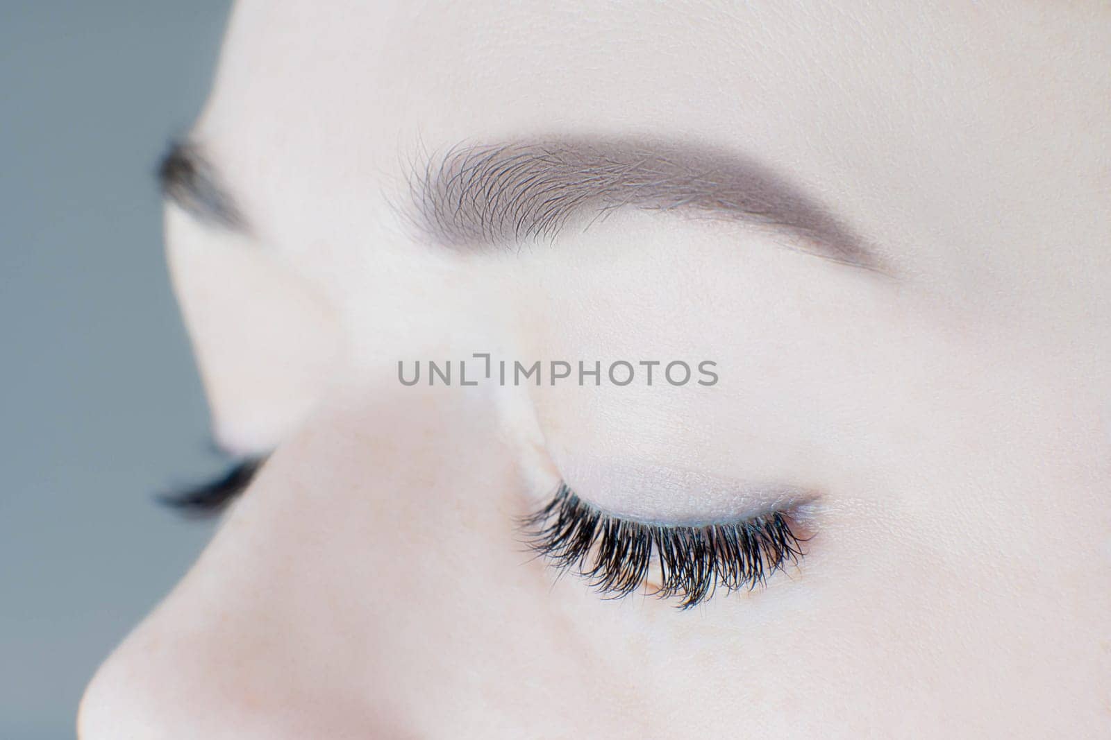 Close-up of closed eyes with long false eyelashes, perfect skin, flawless eyebrows of unrecognizable young woman. Macro shot. Eyelash extension, beauty procedures, cosmetology, visage, microblading.