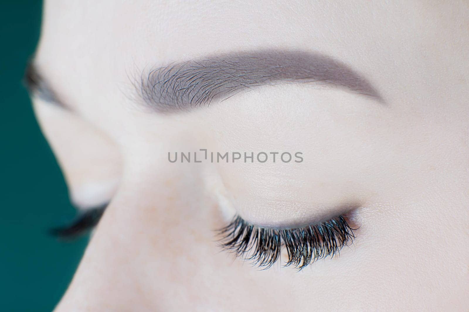 Close-up of closed eyes with long artificial eyelashes, perfect black eyeliner, ideal skin, beautiful eyebrows of unrecognizable young woman. Macro shot. Beauty procedures, cosmetology, microblading.