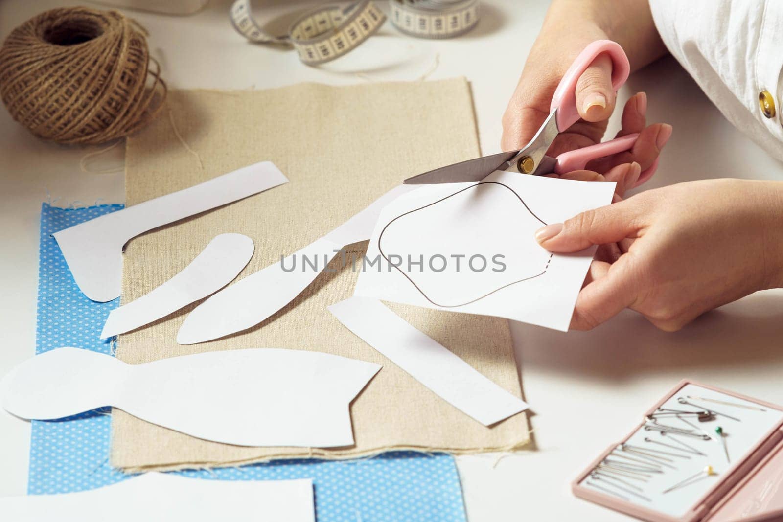 Cropped female designer hands cutting out different shapes, patterns from paper for future clothes and toy sewing project in workshop. Handcraft, do it yourself tutorial. Needlework and manufacture