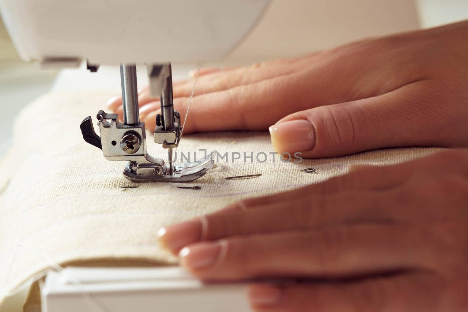 Unrecognizable cropped female dressmaker hands putting white soft fabric textile with stitch contour sewing pattern on sewing machine needle plate under shearer fork. Clothes production in workshop