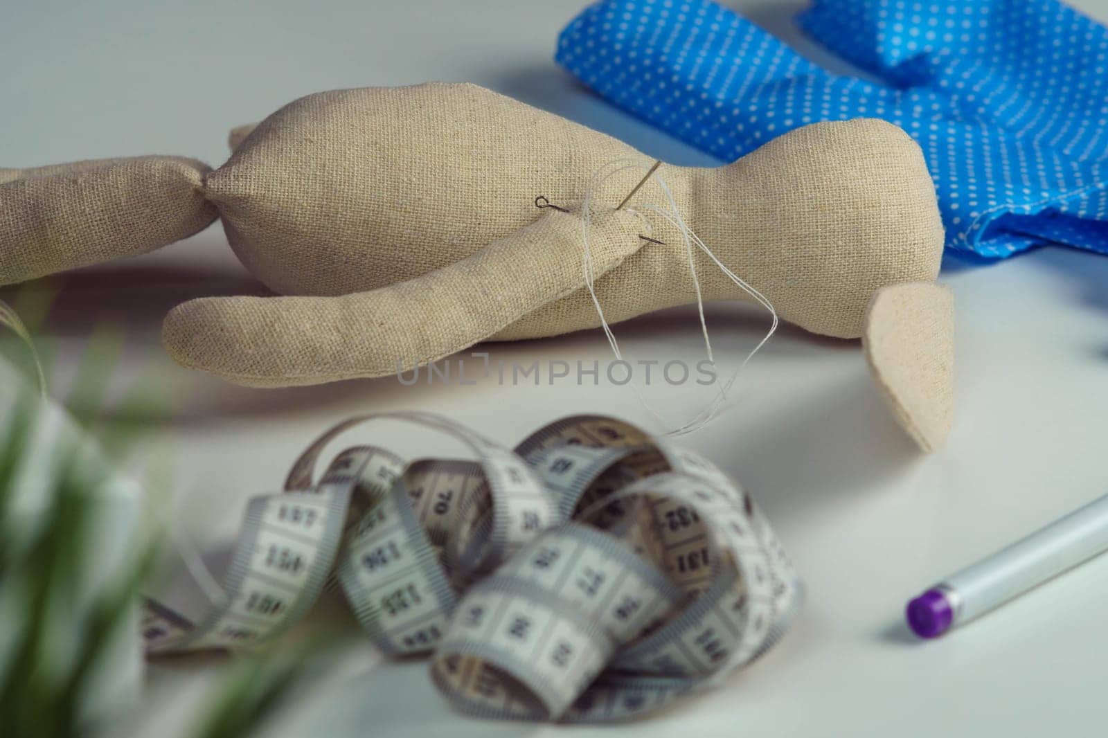 Sewing process of stuffed rabbit toy with needles in body lying on table. Knitting hobby. Hare toy near blue polka dot textile near measure tape and marker. Toys shop, store. DIY, children present