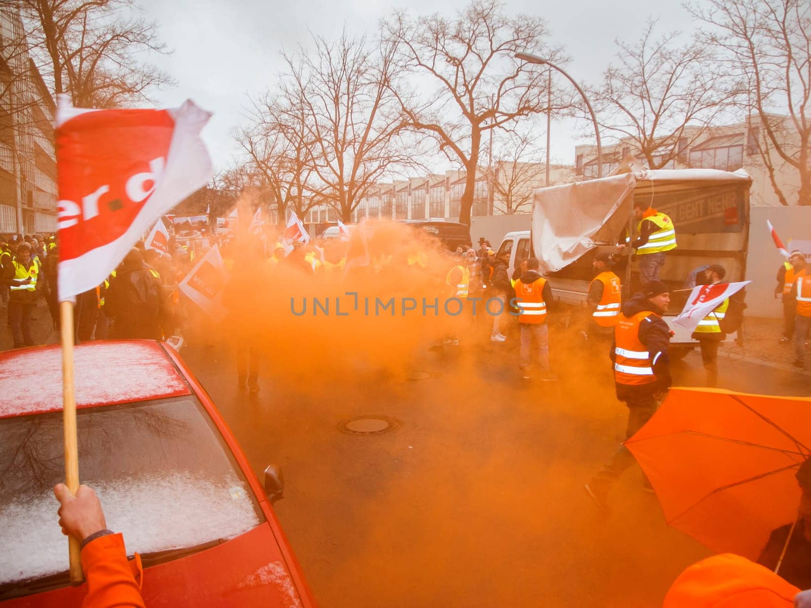 Berlin, Germany - March 06, 2023: Warning strike in front of the gates of the Berliner city cleaning company with orange smoke and waving flags of the union Verdi.