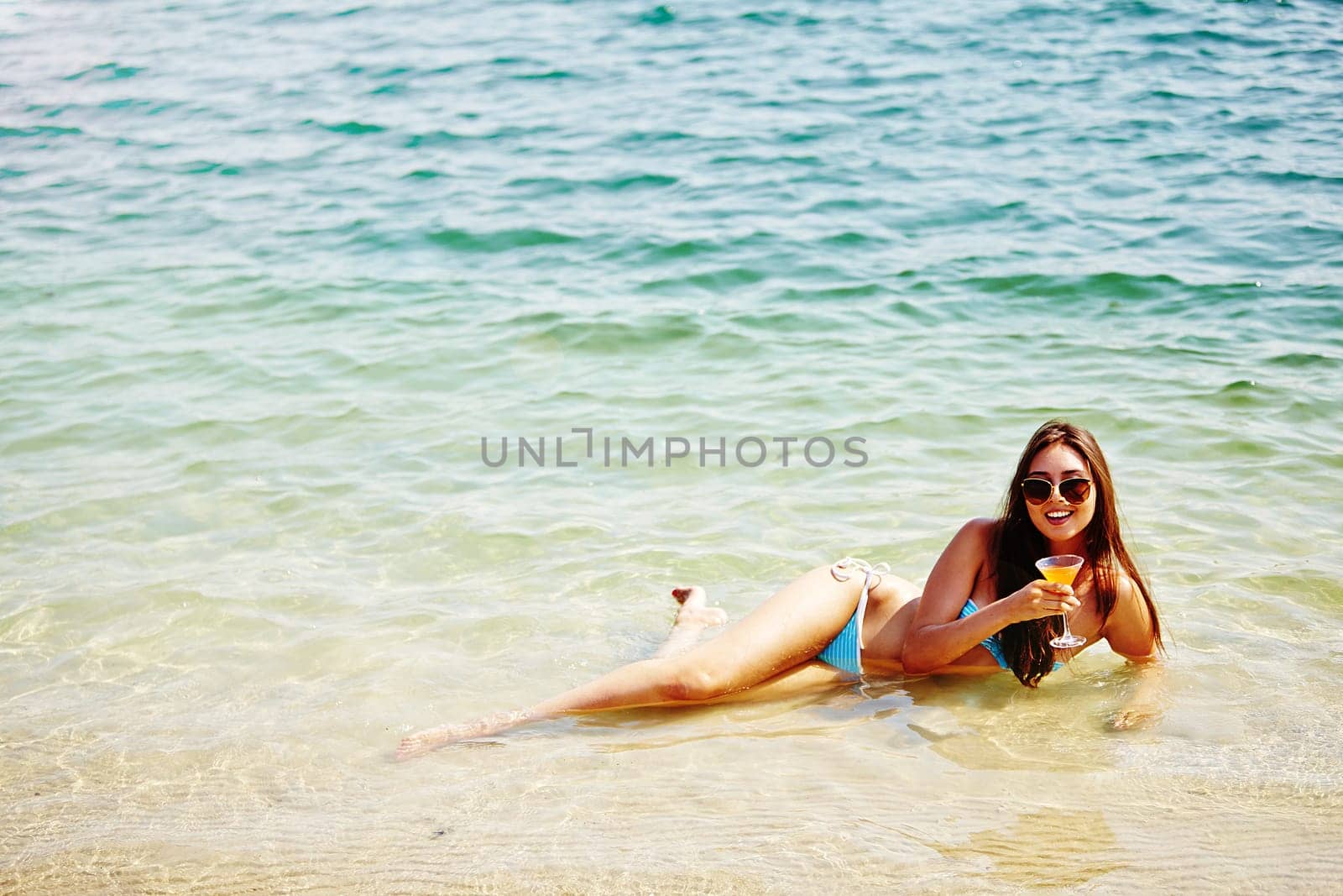 Happy young woman with cocktail lying in water