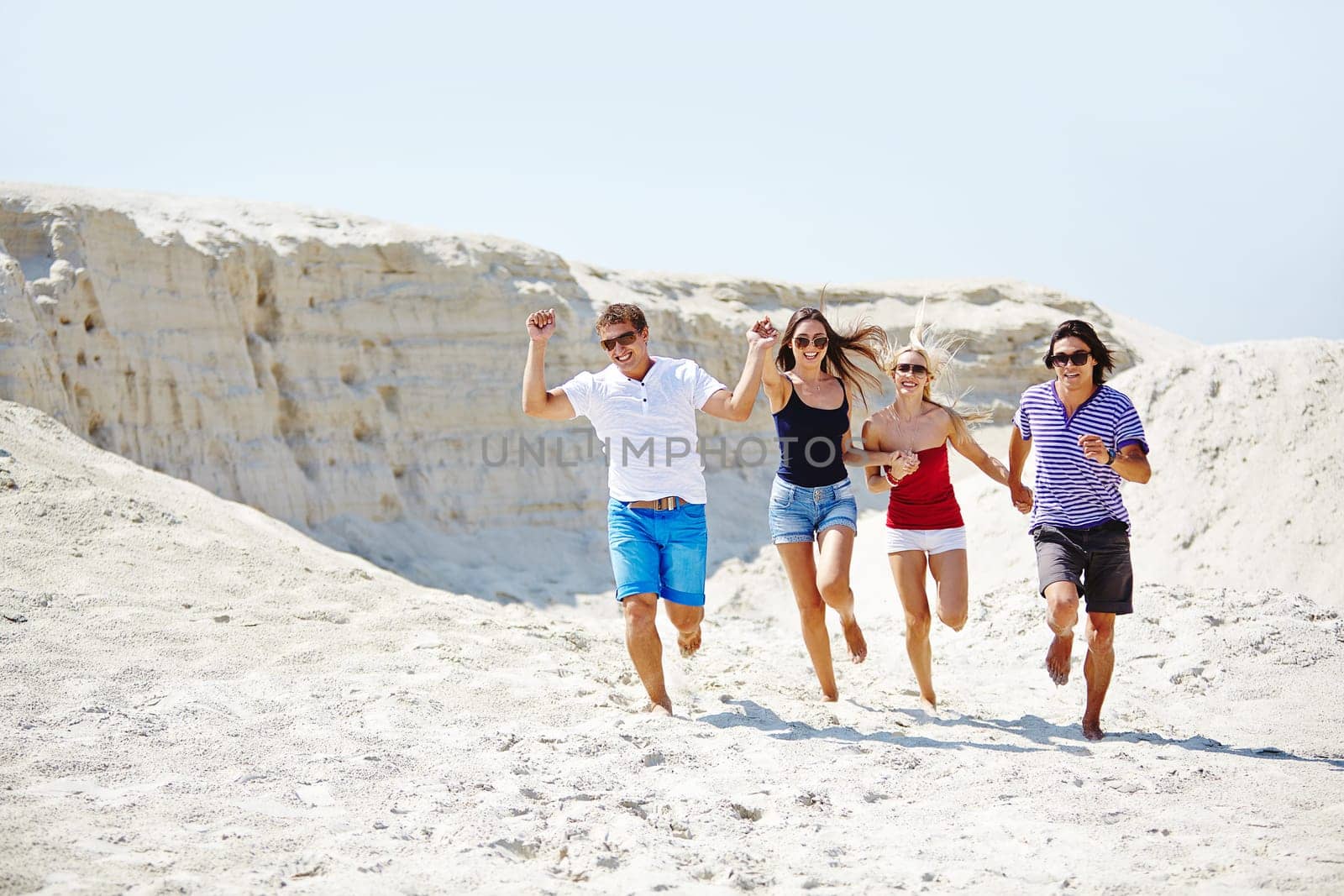 Happy friends running down sandy beach on hot day