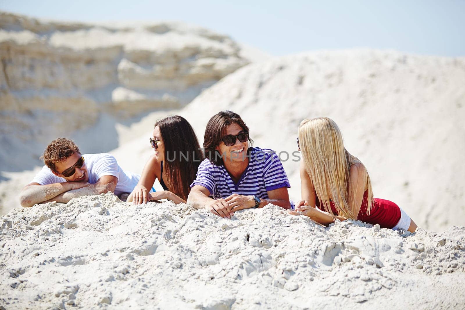 Happy friends in sunglasses relaxing on sand
