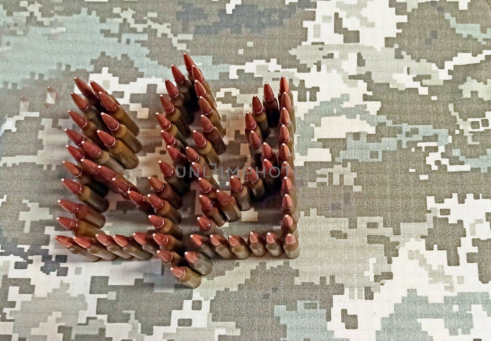 coat of arms of Ukraine laid out from cartridges against background of camouflage clothing. Cartridges for the Kalashnikov assault rifle. War Concept. Pile of bullets. Ukrainian national symbol