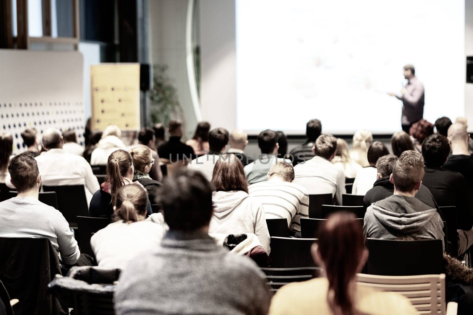 Speaker giving a talk in conference hall at business event. Audience at the conference hall. Business and Entrepreneurship concept. Focus on unrecognizable people in audience.