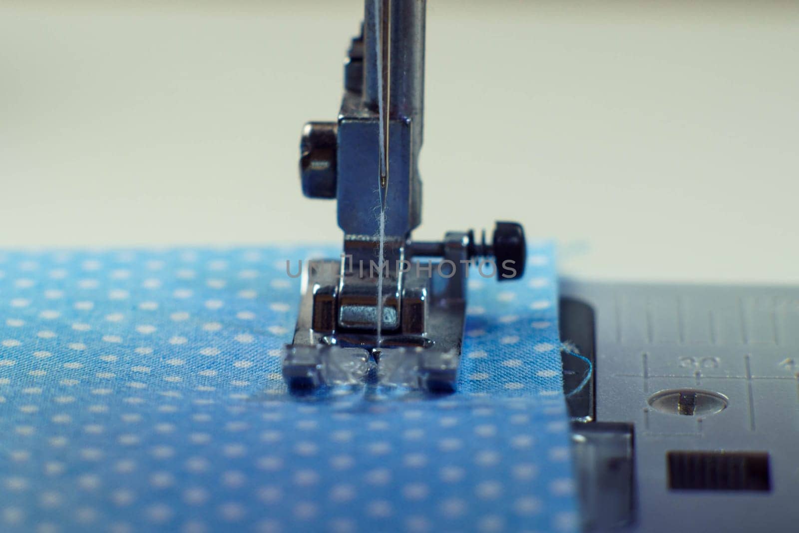 Detailed close up shot of sewing machine steel foot with needle and thread stitching on blue fabric polka dot textile. Sewing machine, tailor's shop, atelier, dressmaker industry. Needle craft