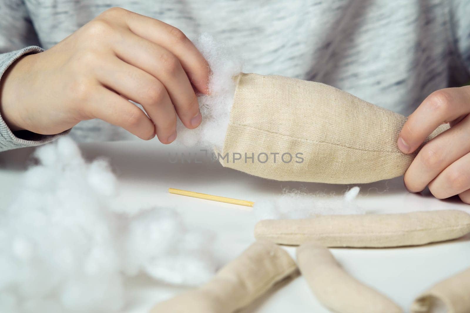 Unrecognizable closeup of woman designer hands sewing soft toys. Create paws and body part, stuffed them with cotton on table. Kid present shop, store. Small business, creative occupation and tutorial