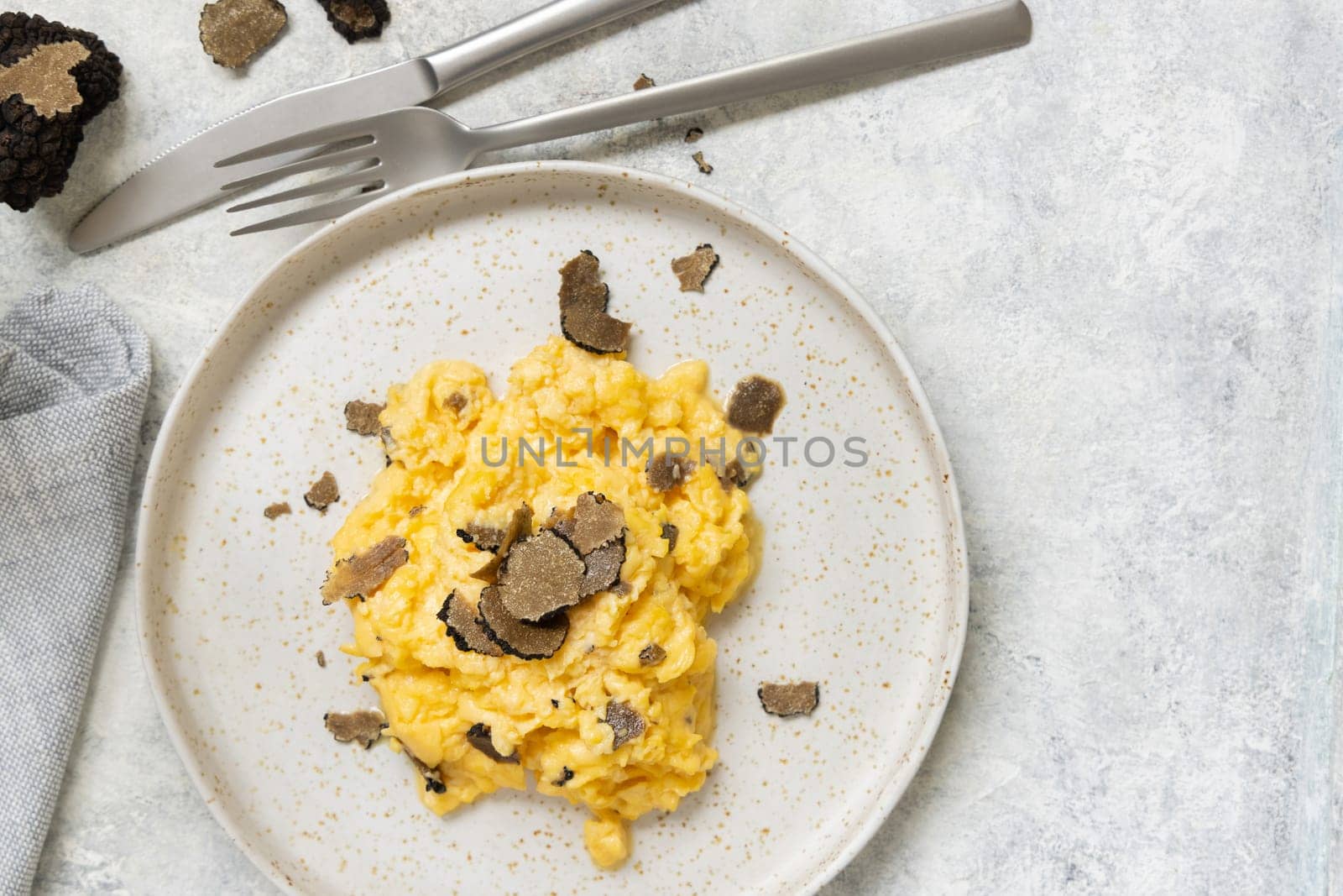 Scrambled eggs with sliced fresh black truffles from Italy served in a plate near fork and knife top view. Italian cousine, gourmet breakfast