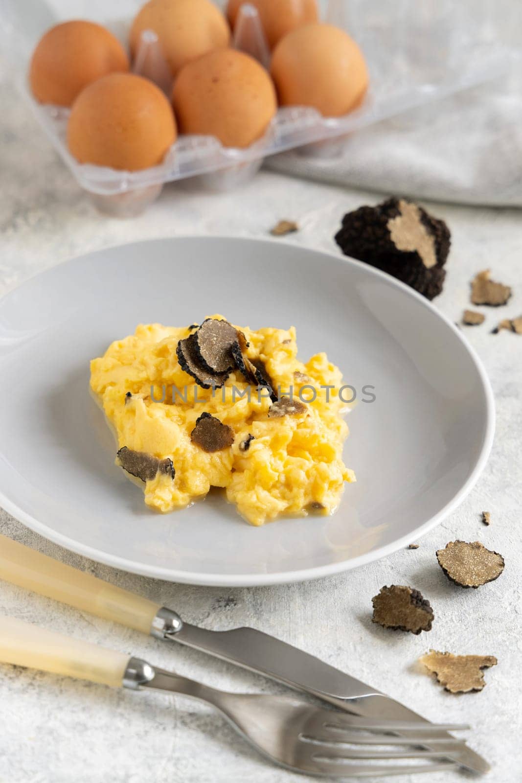 Scrambled eggs with sliced fresh black truffles from Italy served in a plate near fork and knife close up. Italian cousine, gourmet breakfast