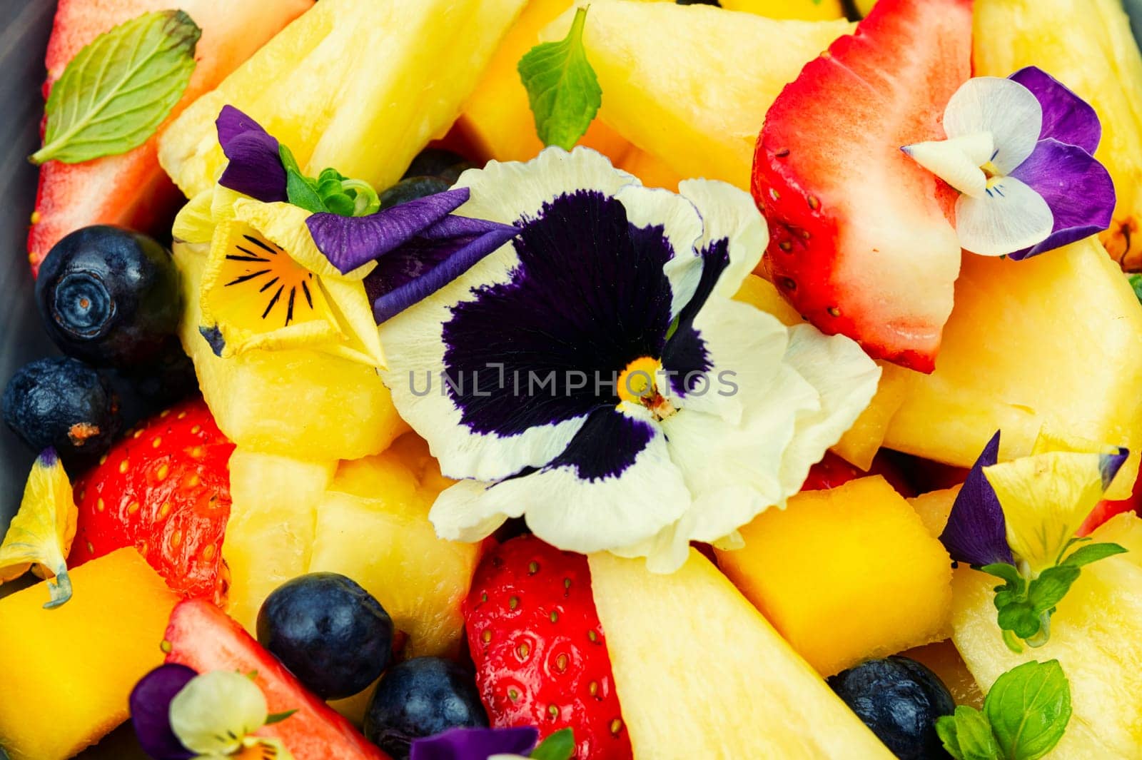 Fresh salad of pineapple, strawberries and berries, decorated with edible flowers.Copy space.