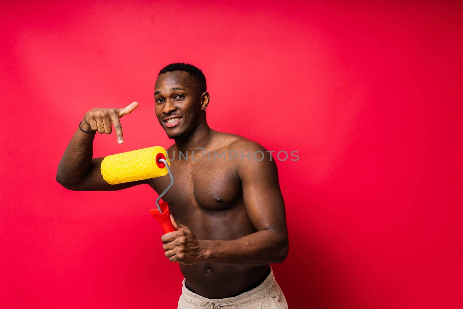 African painter focused on work holding professional roller to paint interior wall, studio.