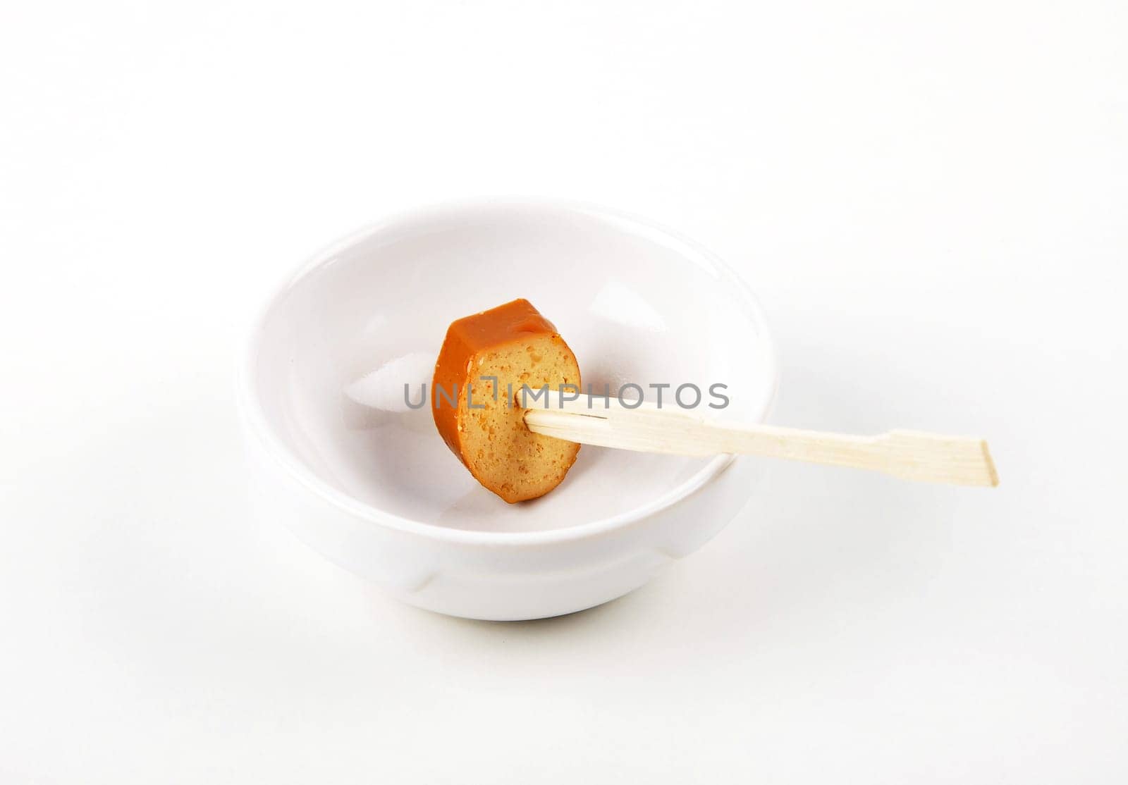 Slice of tofu sausage on wooden skewer in porcelain bowl on white background