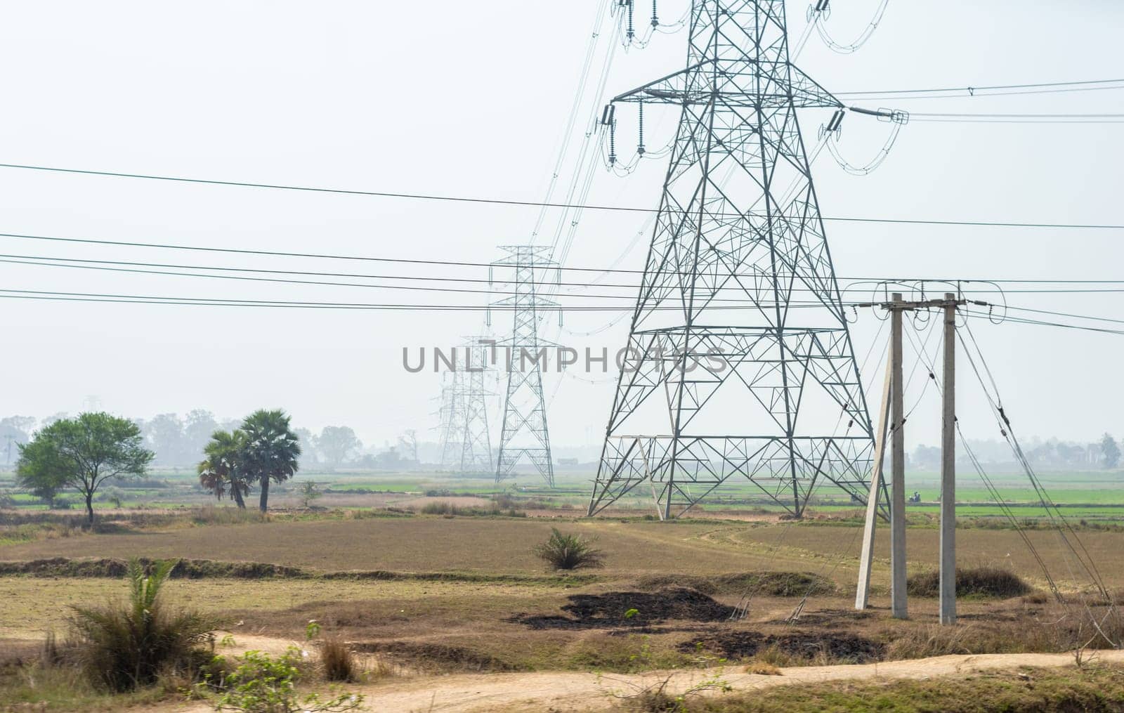 Power lines over an agricultural field against clear sky horizon. High-voltage tower installed in a row on a field.