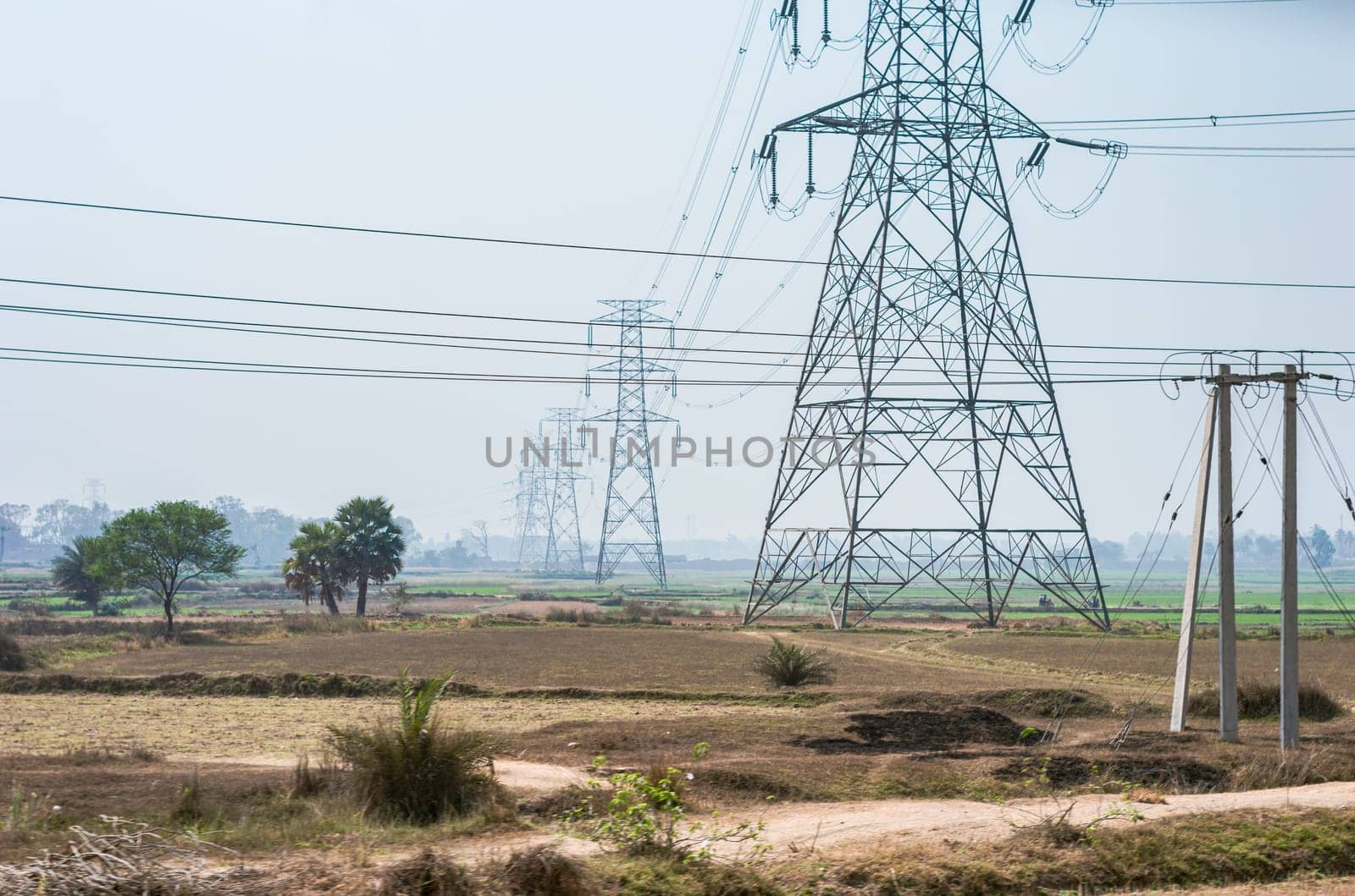 Power lines over an agricultural field against clear sky horizon. High-voltage tower installed in a row on a field.