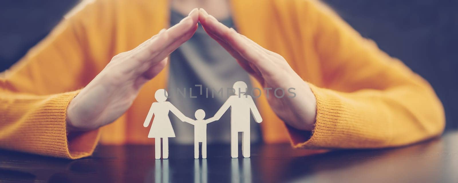 Woman holding her hands in the form of a roof over the figurines of a family.Concept of the care and security in relation.