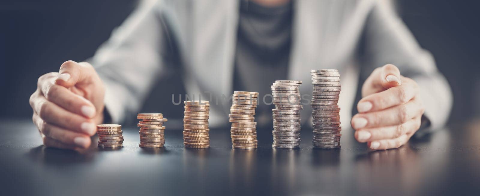 Woman sitting at the table and holding hands around the columns of coins. Concept of the global business and money savings.