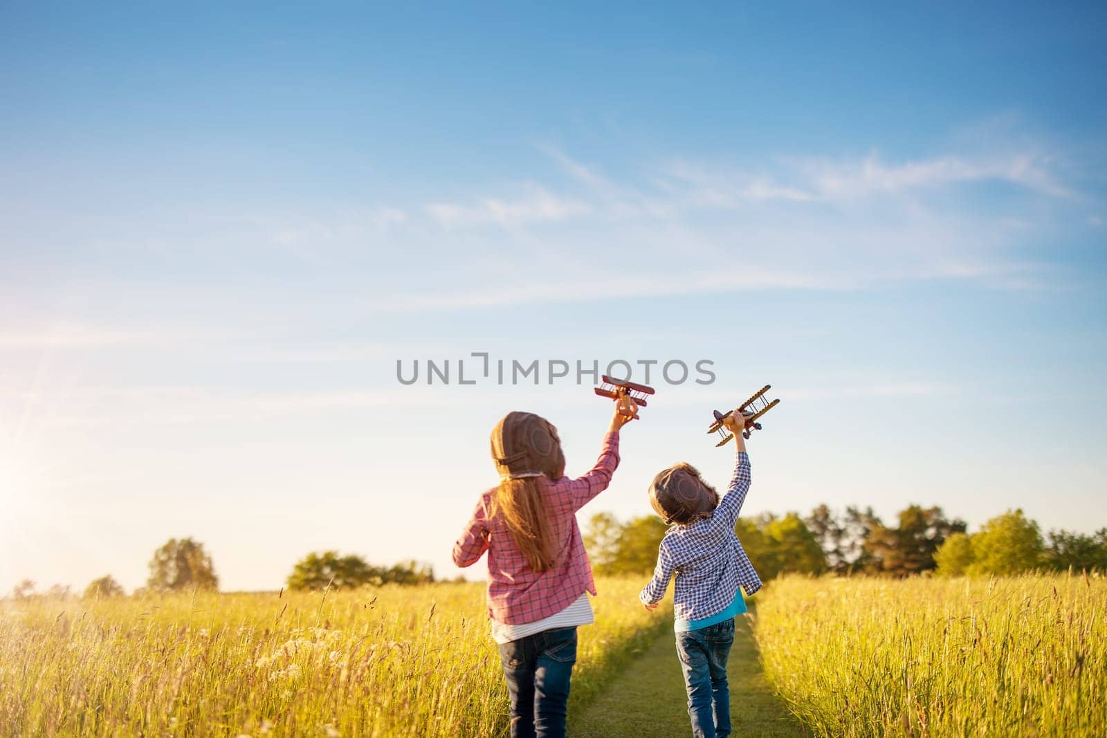 Boy and girl plaing with wooden planes on the field in sunset. Concept of the family vacation, dreaming and friendship.