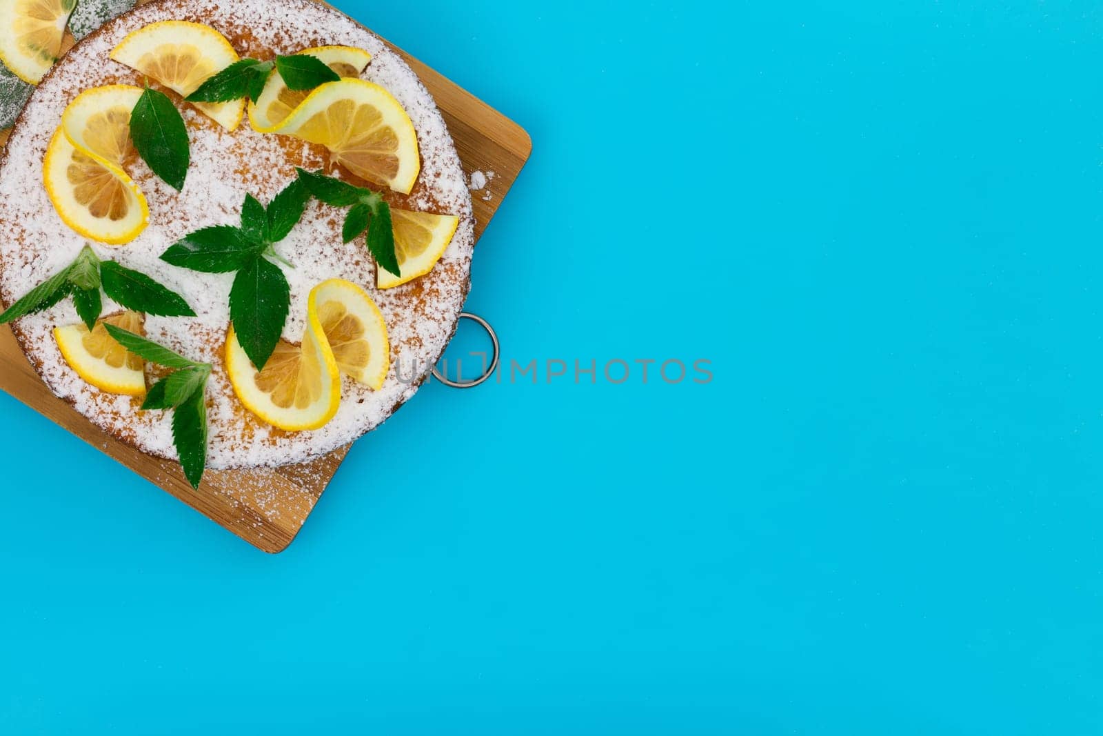 Lemon pie with lemon slices, mint and powdered sugar on a blue background. Top view, copy space.