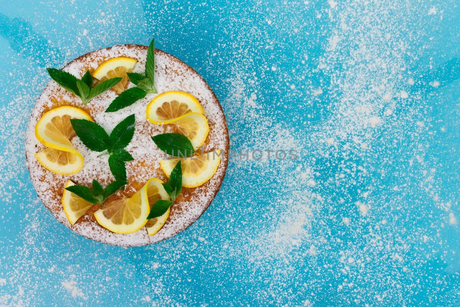 Lemon pie with lemon slices, mint and powdered sugar on a blue background. Top view, copy space.