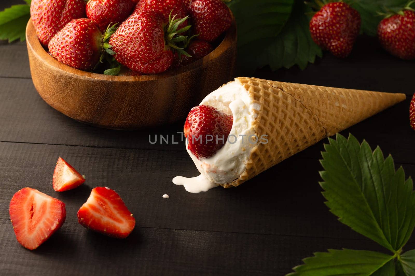 Ice cream and wooden bowl of fresh red ripe strawberries on a black wooden surface. Low key.