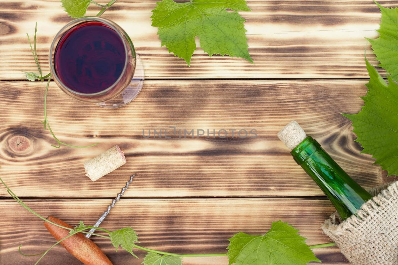 Wine glass, corkscrew, corks, wine bottles, grapevine on rustic burnt wooden background. Top view, copy space
